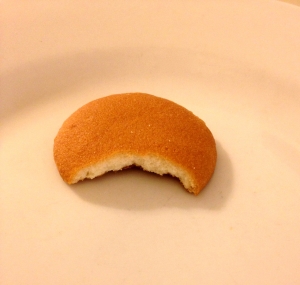 A vanilla wafer, a small, light brown, disk shaped cookie, with a bite taken out of it
